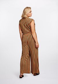 Twee-delig outfit met verticale strepen in groen, oranje en goud. De top is mouwloos met een riem, en de broek heeft wijde pijpen.