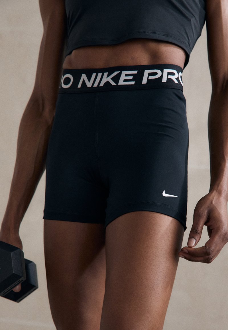 Sorte Nike Pro shorts lavet af strækbart stof, med en høj talje og "Nike Pro" i hvid, samt et lille hvidt logo på benet.