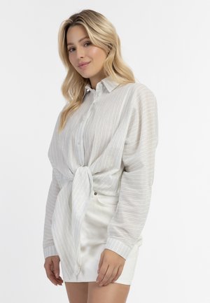 Lightweight, striped button-up shirt in pale blue and white, featuring a tied front and long sleeves. Worn over a white skirt.