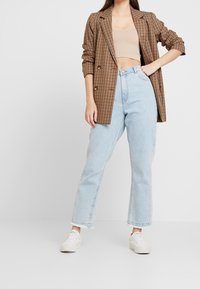 Brun rutig blazer över en beige crop top, i kombination med ljusblå högmidjade vida jeans och vita sneakers.