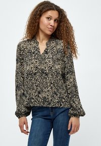 Blusa nera e beige a fantasia con scollatura a V, maniche ampie e tessuto strutturato, abbinata a jeans blu.