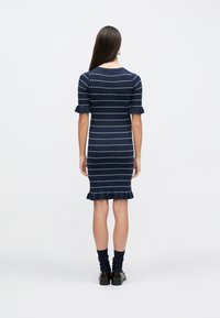 Πλεκτό φόρεμα σε ναυτικό μπλε με λευκές οριζόντιες ρίγες, κοντά σκουλαρίκια με βολάν και εφαρμοστή γραμμή, που τελειώνει λίγο κάτω από τα γόνατα.