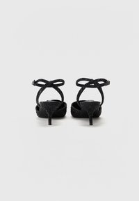 Sandales à talons noirs avec une texture pailletée, des brides croisées et une petite sangle à boucle sur la cheville. Présente un talon aiguille élancé.