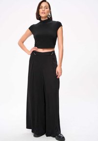 Zwarte crop top met korte mouwen, gecombineerd met hoge taille zwarte wijde broek met een riem met zilveren ringen en plooien.