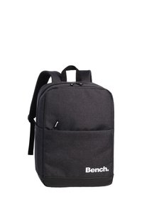 Sac à dos en tissu noir de forme rectangulaire, avec une poche avant, des bretelles rembourrées et un logo imprimé en blanc en bas.