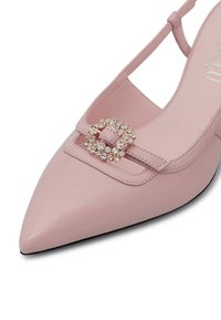 Scarpa in pelle rosa a punta con una fibbia decorativa in strass. Presenta un design con schienale aperto e cinturino alla caviglia. Texture liscia.