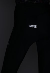 Svarta träningstights med en åtsittande design, slät textur och reflekterande "GORE"-logotyp på vänster ben.