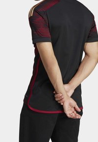 Musta pelipaita punaisilla korostusraidoilla, lyhyillä hihoilla ja ribbauskauluksella. sisältää hienovaraisia kuvioita hartioilla ja punaisissa kylkisaumoissa.