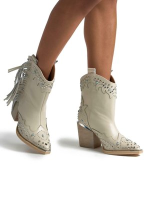 Stivali da cowboy in pelle beige con frange, borchie argentate e punta affusolata. Presentano un tacco in legno impilato e un accento metallico sulla punta.