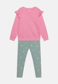 Felpa di cotone rosa con dettagli a balza sulle spalle, abbinata a leggings verdi con un motivo floreale in rosa e giallo.
