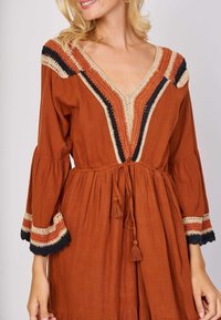 Rust-colored dress with a V-neck, bell sleeves, and decorative crocheted accents in black and beige. Drawstring waist with tassels.