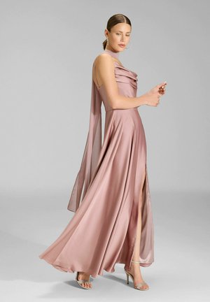 Floor-length dress in soft pink satin with draped bodice, one shoulder strap, and a thigh-high slit; paired with silver high-heeled sandals.