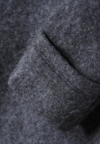 Mörkgrå ulltyg med en mjuk, texturerad yta. Har en vikt manschettdetalj som framhäver tjockleken och materialkvaliteten.