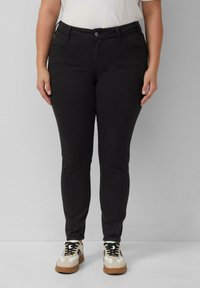 Čierne džínsy s priliehavým strihom, vyrobené z denimu, s piatimi vreckami, so zapínaním na gombík a jemnou, hladkou textúrou. Skombinované s bielymi teniskami.