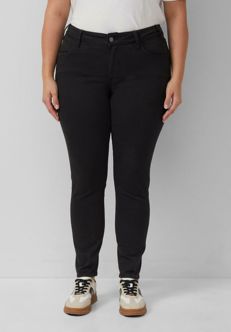 Čierne džínsy s priliehavým strihom, vyrobené z denimu, s piatimi vreckami, so zapínaním na gombík a jemnou, hladkou textúrou. Skombinované s bielymi teniskami.