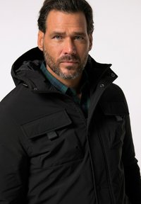 Schwarze Parka-Jacke mit Kapuze, mehreren Fronttaschen und strukturiertem Stoff. Ausgestattet mit einem Reißverschluss und Druckknöpfen.