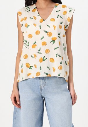 Weißes ärmelloses Oberteil mit V-Ausschnitt, durchgehend mit einem orangefarbenen Blattmuster versehen. Kombiniert mit hellblauen Denim-Jeans.