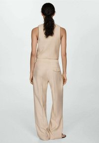 Tenue beige en tissu côtelé composée de deux pièces, comprenant un haut sans manches et un pantalon à jambes larges. Le pantalon présente un détail de poche arrière.