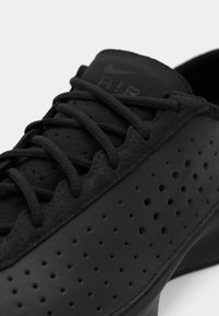 Pantof lung cu aspect sport în negru, având un material texturat, un design perforat și șireturi plate. Pantoful are un finisaj neted și un logo discret pe limbă.