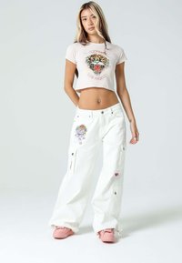 Hvide cargo bukser med dekorativ broderi og lommer, parret med en lys pink cropped t-shirt med et tiger motiv. Pink fodtøj inkluderet.