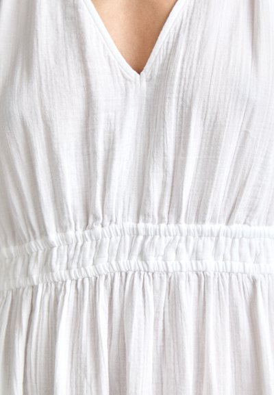 Robe blanche avec décolleté en V, taille froncée et texture fluide. Fabriquée en tissu léger avec des plis subtils et doux sur l'ensemble.