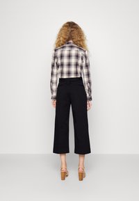 Koszula w kratę z długimi rękawami, czarne szerokie spodnie i beżowe buty na platformie. Tkanina o fakturze z wzorem w kratę, neutralna paleta kolorów.