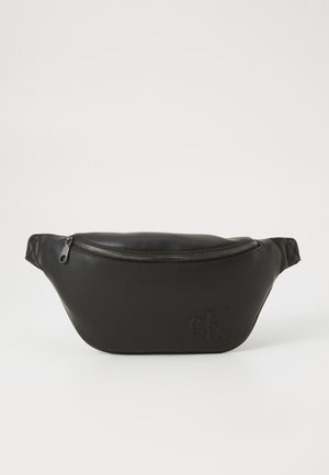 Musta nahkavyölaukku vetoketjukiinnityksellä ja kohokuvioidulla "cK"-logolla edessä, esitetty yksinkertaisella valkoisella taustalla.