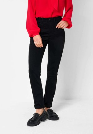 Persoon die zwarte slim-fit broek draagt, zwarte loafers met franjerand en een felrode blouse met lange mouwen en omgeslagen manchetten.