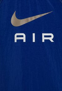 Blå träningslinne med en stor guldig Nike swoosh-logotyp och vit "AIR" text, strukturerad tyg med en slät finish.