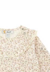 Bluse aus hellcremefarbenem Stoff mit Blumenmuster, Rüschensaum, Druckknöpfen und einem strukturierten Teddy-Bär-Detail am Ärmel. Größenetikett angebracht.