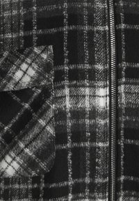 Tela de cuadros en blanco y negro con una solapa de bolsillo doblada a la izquierda y una cremallera metálica a la derecha.