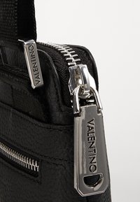 Svart läderhandväska med silverdetaljer, texturerad yta och dragkedjestängning med en märkt dragkedja och litet ytterfack.