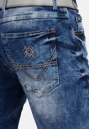 Spijkerbroeken in een lichte tot donkere blauwe wassing. Bevat geborduurde details op de achterzakken en gele stiksels langs de naden.