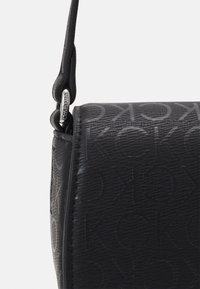 Borsa a tracolla nera con motivo a logo embossato, pelle texture e un accento in metallo argentato sulla tracolla per una lunghezza regolabile.