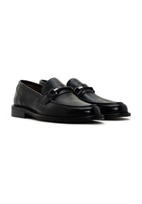 Mocasines de cuero negro con un acabado texturizado, que presentan un diseño elegante, una suela plana y un acabado de hebilla metálica en la parte frontal.