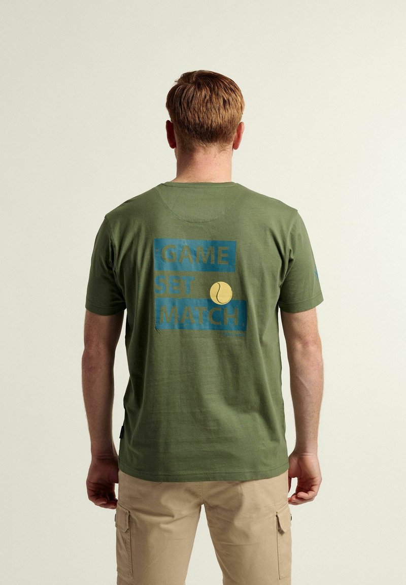 Camiseta de algodón verde con un estampado gráfico azul en la parte trasera que incluye el texto "GAME SET MATCH" y un icono de bola de tenis amarilla.