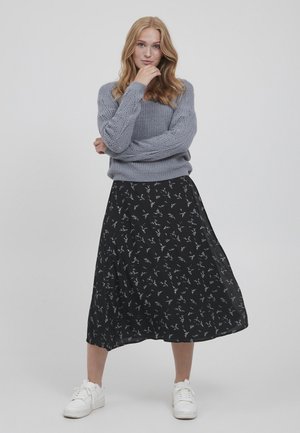 Grauer gestrickter Pullover mit einem strukturierten Muster, kombiniert mit einem schwarzen Midikleid mit Blumenmuster. Weiße Sneakers vervollständigen das Outfit.