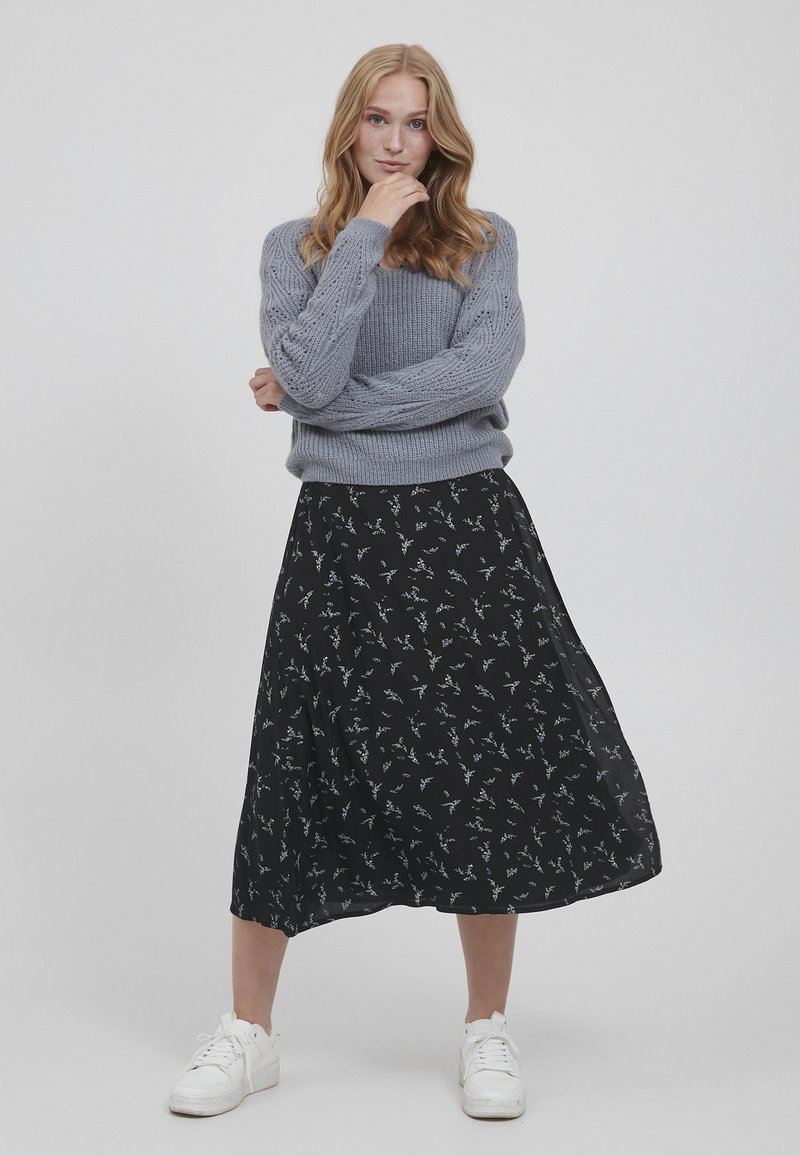 Pulover gri tricotat cu un model texturat, asociat cu o fustă midi neagră cu imprimeu floral. Tenisii albi completează ținuta.