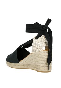Black fabric espadrille wedge with a woven cream accent, an ankle tie, and a textured jute platform. Open heel design.