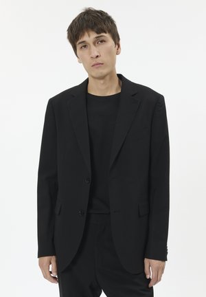 Giacca nera in tessuto liscio, con un design classico caratterizzato da revers a punta, due bottoni e tasche laterali. T-shirt nera casual.