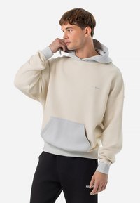 Beige fleecetrui met een grijze capuchon en zak, voorzien van geribbelde boorden en een klein logo op de borst. Zachte textuur en een losse pasvorm.