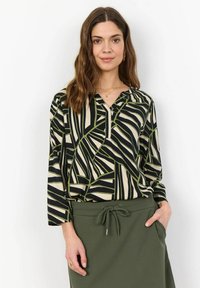 Blouse à manches longues en noir, crème et motif géométrique vert, avec un col en V et une coupe décontractée, associée à une jupe verte assortie.
