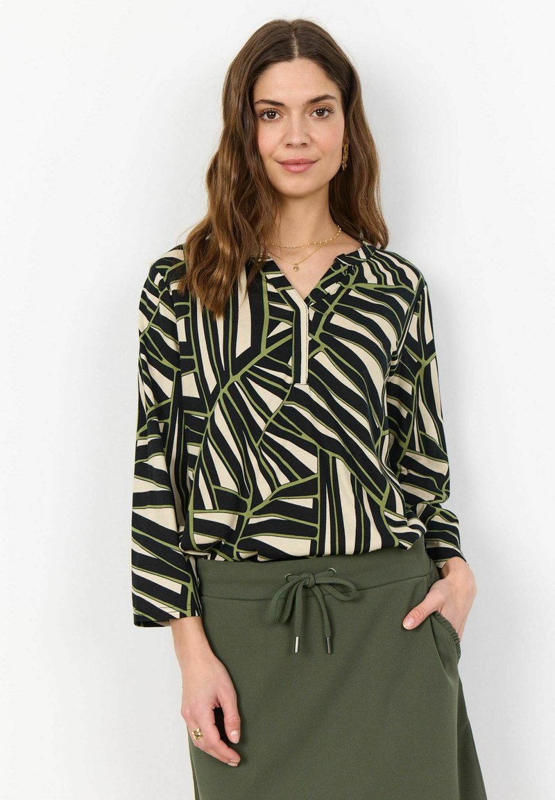 Blouse à manches longues en noir, crème et motif géométrique vert, avec un col en V et une coupe décontractée, associée à une jupe verte assortie.