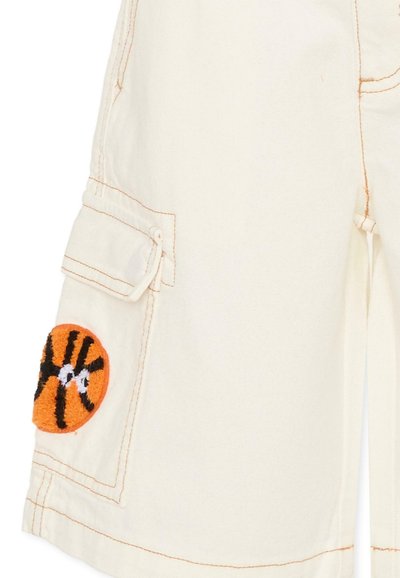 Pantalon beige avec surpiqûres orange et une poche latérale ornée d'un patch de basket-ball texturé orange et noir.