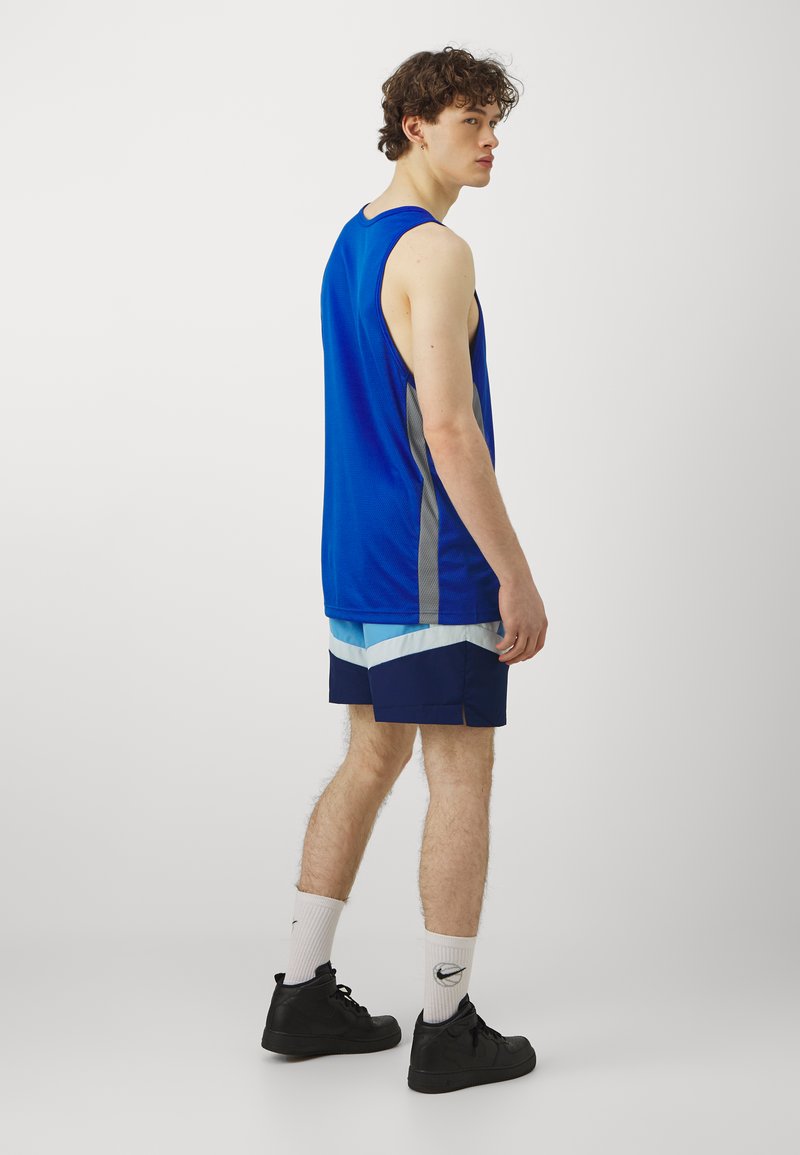 Outfit sportivo da uomo composto da una canotta blu, pantaloni shorts blu navy e azzurrini, sneaker nere e calze bianche con un logo.
