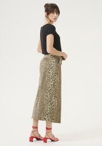 Haut noir à manches courtes associé à une jupe maxi à imprimé léopard. Jupe dans des tons beiges et bruns, avec une taille haute et des sandales rouges à bout carré.