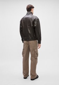 Must must artejak, millel on kõrge krae, koos khaki värvi cargo pükstega, millel on mitu taskut ja millel on vabalt voolav lõige. Sile tekstuur ja kaasaegne disain.