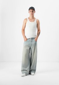 Balts tanktops, gaiši zili plata piegriezuma džinsi ar izbalējušu tekstūru un balti sporta apavi. Melna cepure ar smalku rakstu.