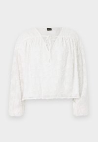 Weiße kurz geschnittene Bluse mit langen Ärmeln, strukturiertem floralen Spitzenmuster, V-Ausschnitt und Schnürdetail an der Vorderseite. Weiches, durchscheinendes Material.