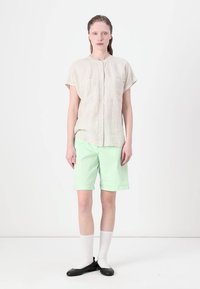 Camicetta a maniche corte di un leggero beige a righe con una piccola tasca, abbinata a pantaloni corti verde menta, calze bianche fino al ginocchio e ballerine nere.